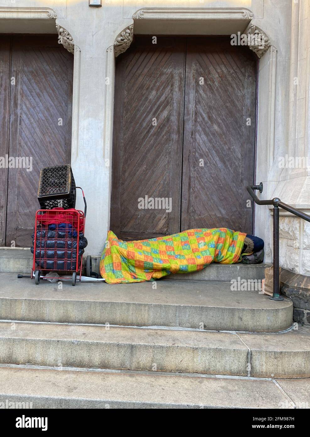 Sans-abri homme avec une courtepointe colorée dort contre les portes d'une église où il se sent en sécurité dans le quartier Park Slope de Brooklyn, New York. Banque D'Images