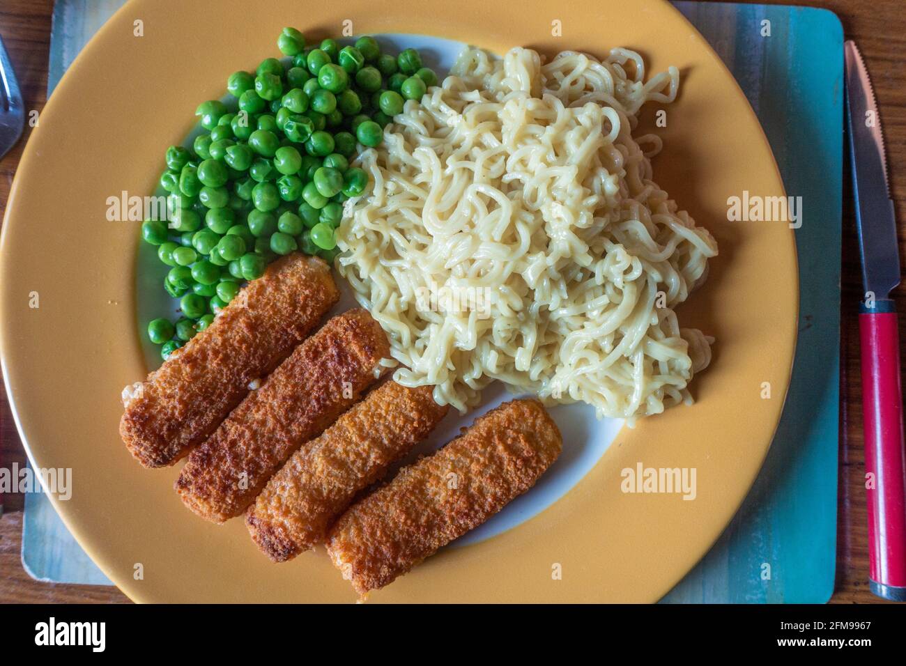 Un repas rapide et facile composé de doigts de poisson, de nouilles instantanées et de pois. Banque D'Images