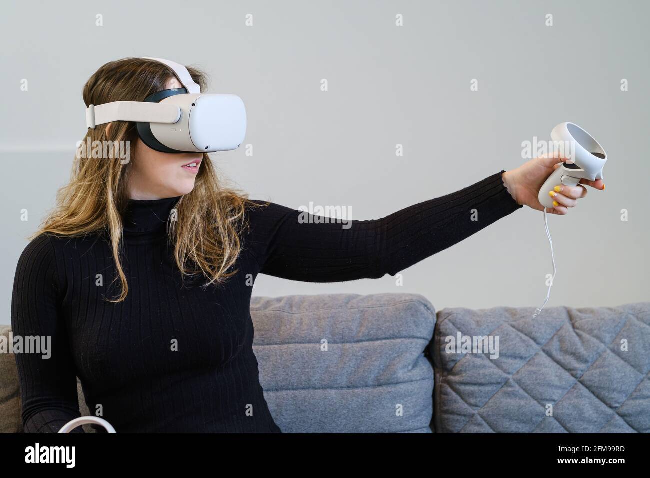 AN, BELGIQUE - 20 avril 2021 : une jeune femme essaie la quête 2 d'Oculus pour une expérience virtuelle. Assis dans un canapé, avec un dessus noir. Banque D'Images