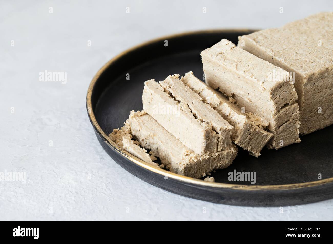Halava tranché dans une assiette noire sur fond blanc. Gros plan sur la halva de tournesol. Dessert de l'est. Banque D'Images