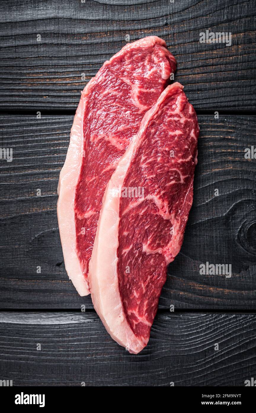 Steak de bœuf cru ou bifteck de viande de bœuf au chapeau de sirloin sur la table de boucher. Arrière-plan en bois noir. Vue de dessus Banque D'Images