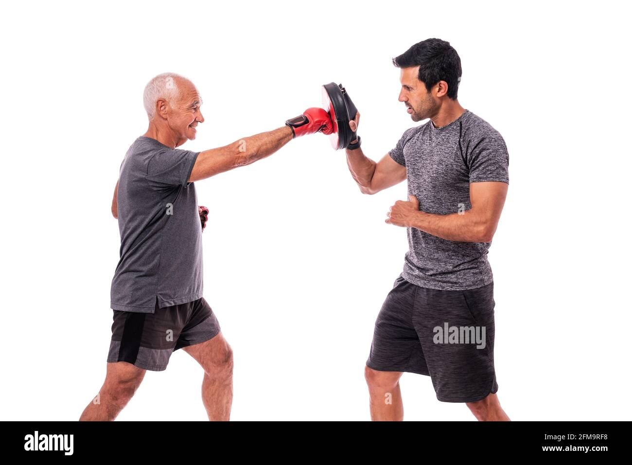 Athlète masculin âgé en excellente forme physique, en gants de boxe, avec un entraîneur de fitness, pratiquant la boxe. Sur un arrière-plan blanc isolé. Banque D'Images