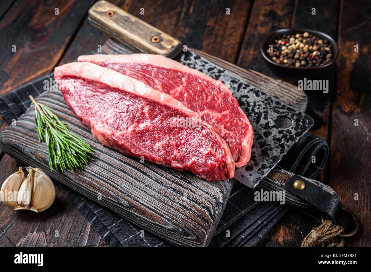 Steaks de viande de bœuf sur le dessus de la cicloine crue sur le butboard avec le cale à viande. Arrière-plan sombre. Vue de dessus Banque D'Images