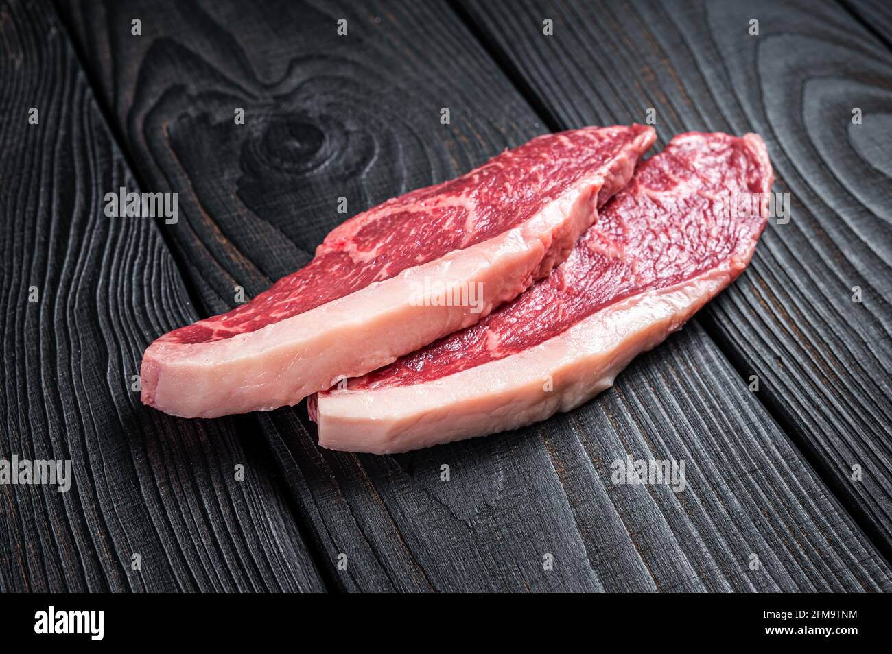 Steak de bœuf cru ou bifteck de viande de bœuf au chapeau de sirloin sur la table de boucher. Arrière-plan en bois noir. Vue de dessus Banque D'Images