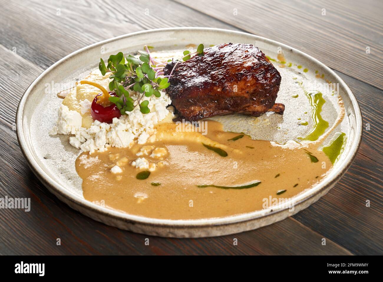Vue rapprochée du steak de bœuf grillé juteux servi avec purée de pommes de terre, fromage cottage, sauce et pousses. Plat savoureux présenté sur une table en bois au restaurant. Concept de cuisine. Banque D'Images