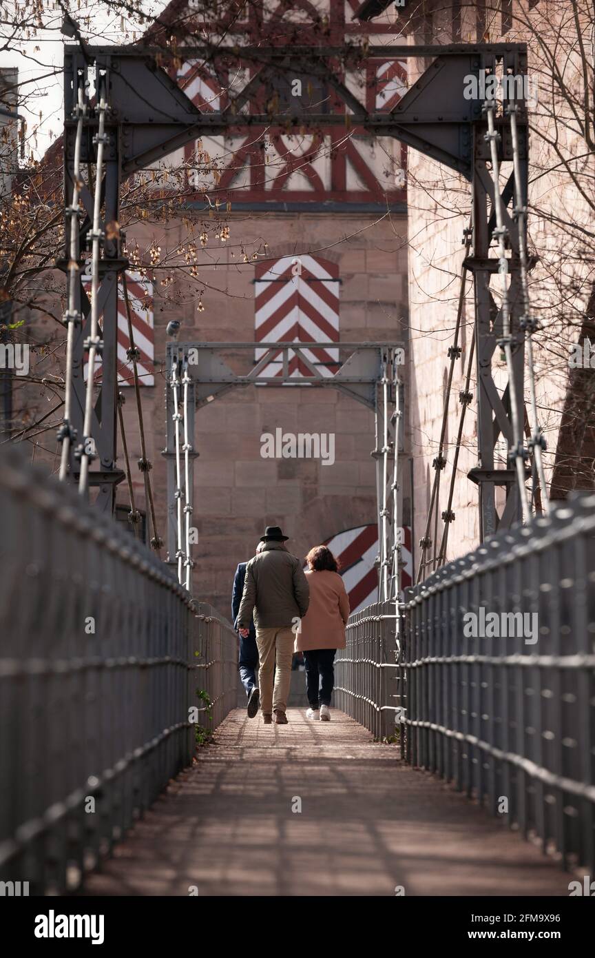 Nürnberg, ALLEMAGNE - 10 mars 2021: Touristes traversant le pont de la chaîne à Nuremberg. Une ancienne maison à colombages / maison en grès peut être vue en t Banque D'Images