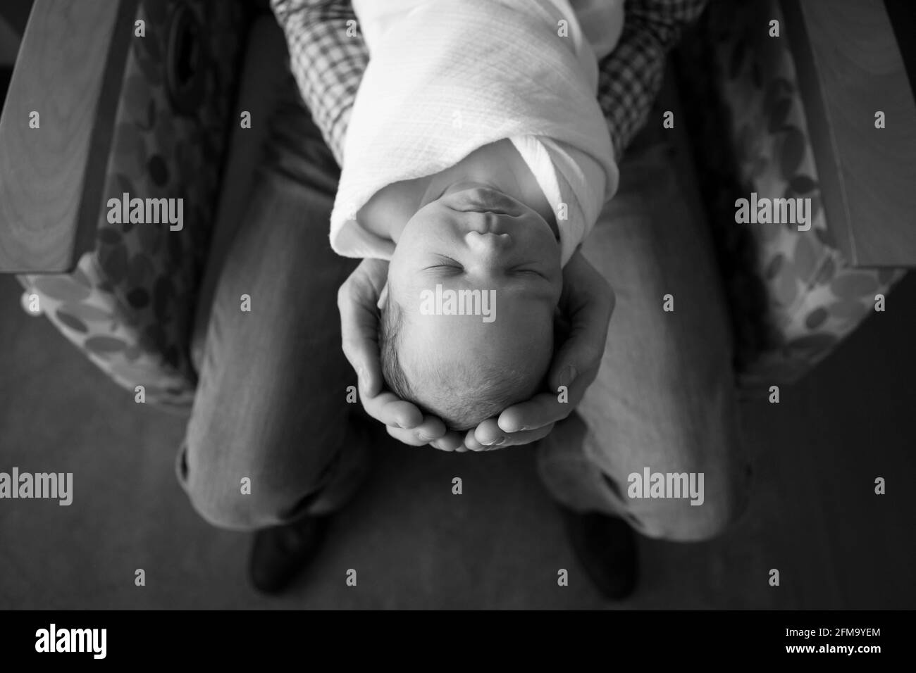 Un père tient un nouveau-né dans les mains tout en étant assis dans une chaise d'hôpital Banque D'Images
