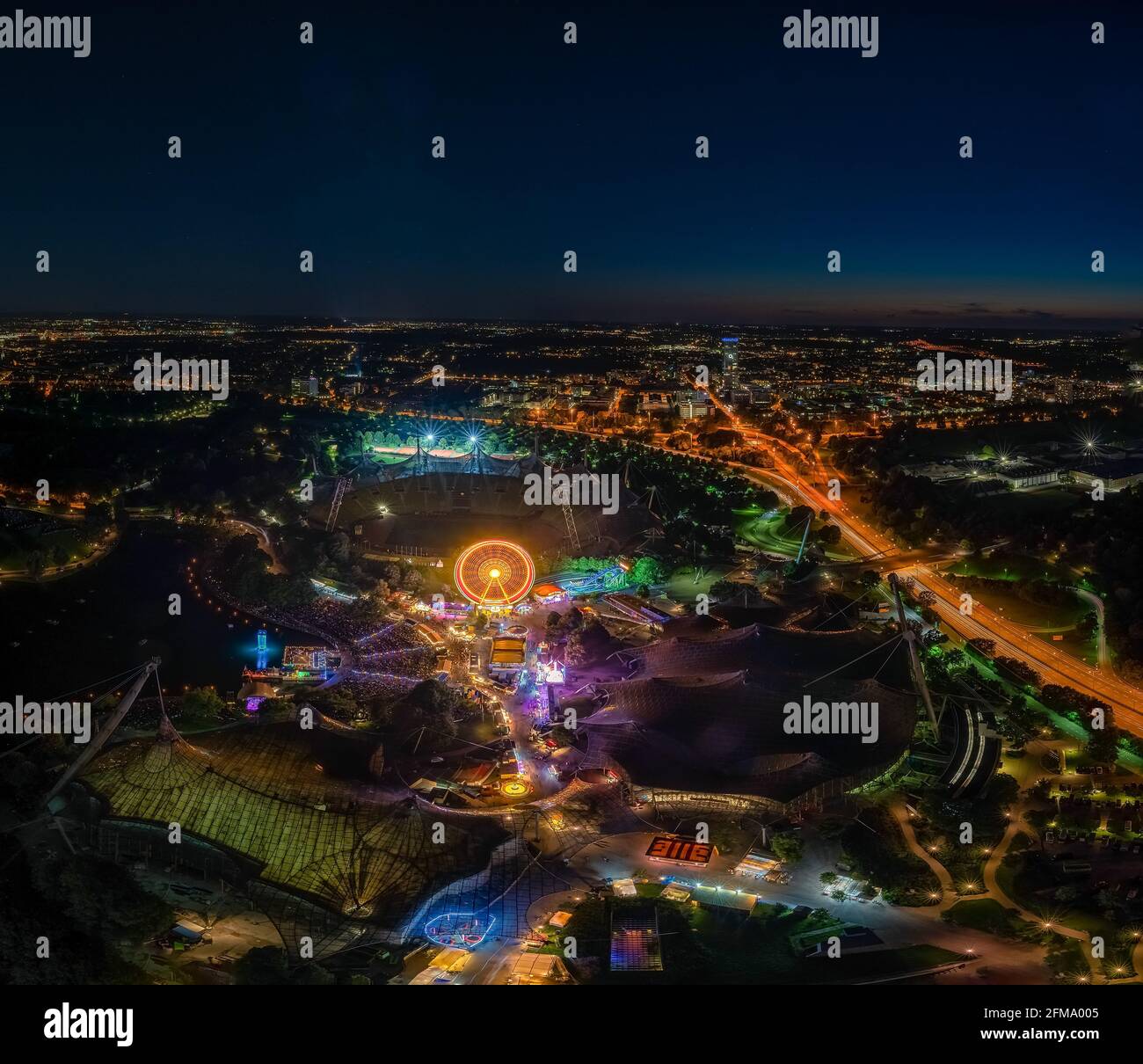 Une impressionnante photo de nuit au-dessus de Munich depuis la Tour Olympique au festival « Impark » la nuit avec une grande roue illuminée. Banque D'Images