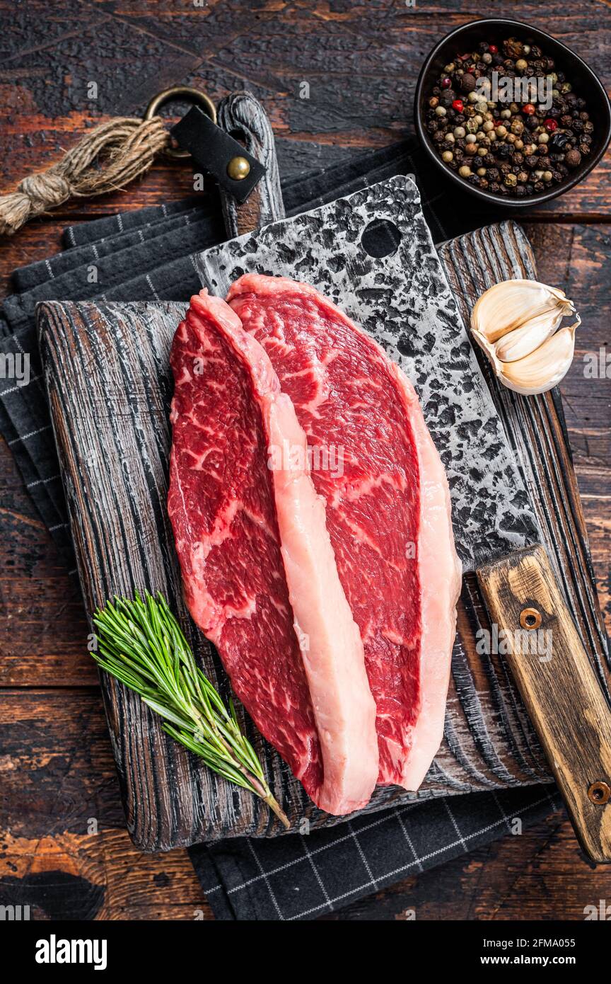 Steaks de viande de bœuf sur le dessus de la cicloine crue sur le butboard avec le cale à viande. Arrière-plan sombre. Vue de dessus Banque D'Images