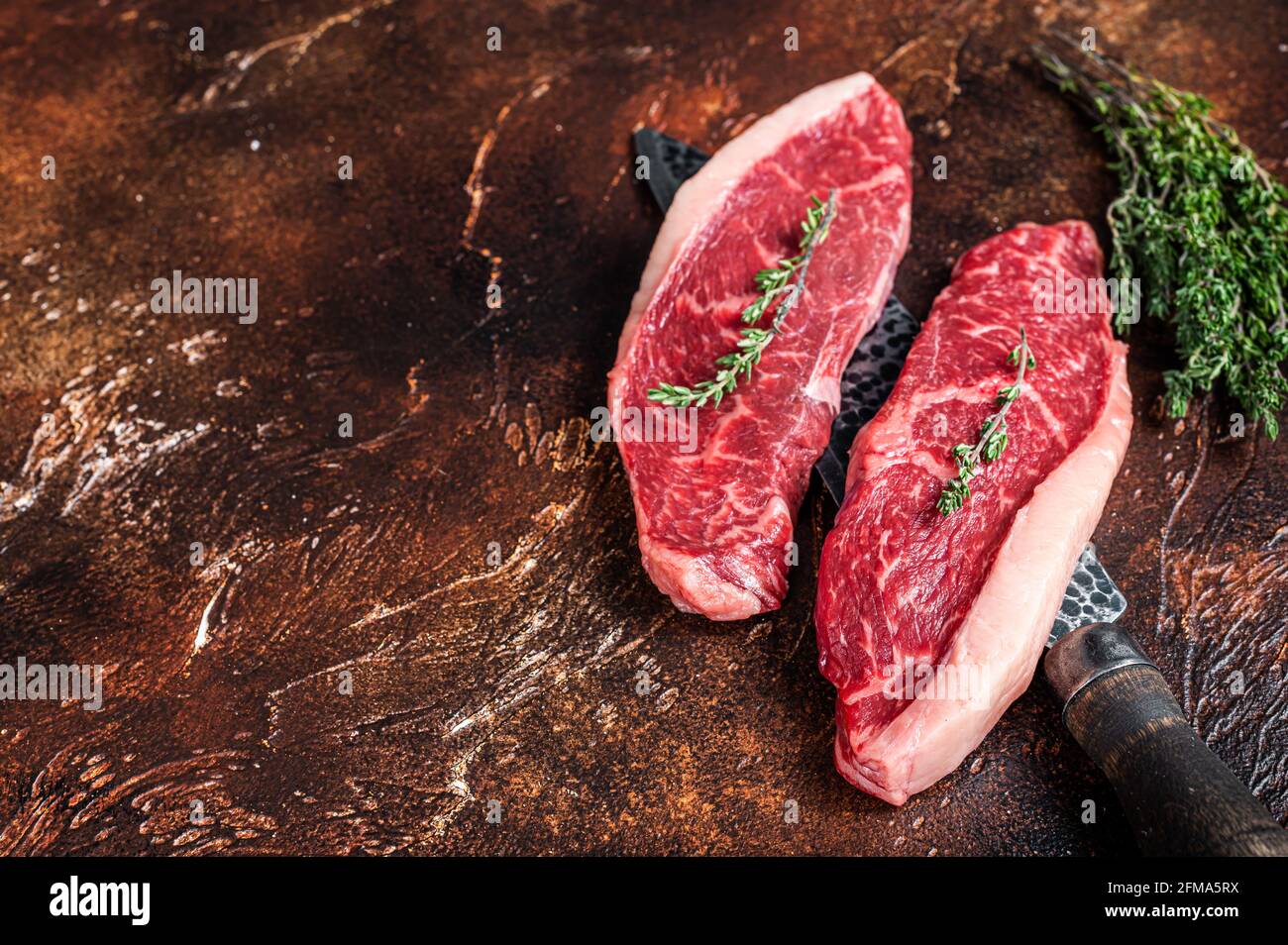 Chapeau de sirloin cru non cuit ou steaks de viande de bœuf sur un couteau de boucher. Arrière-plan sombre. Vue de dessus. Copier l'espace Banque D'Images