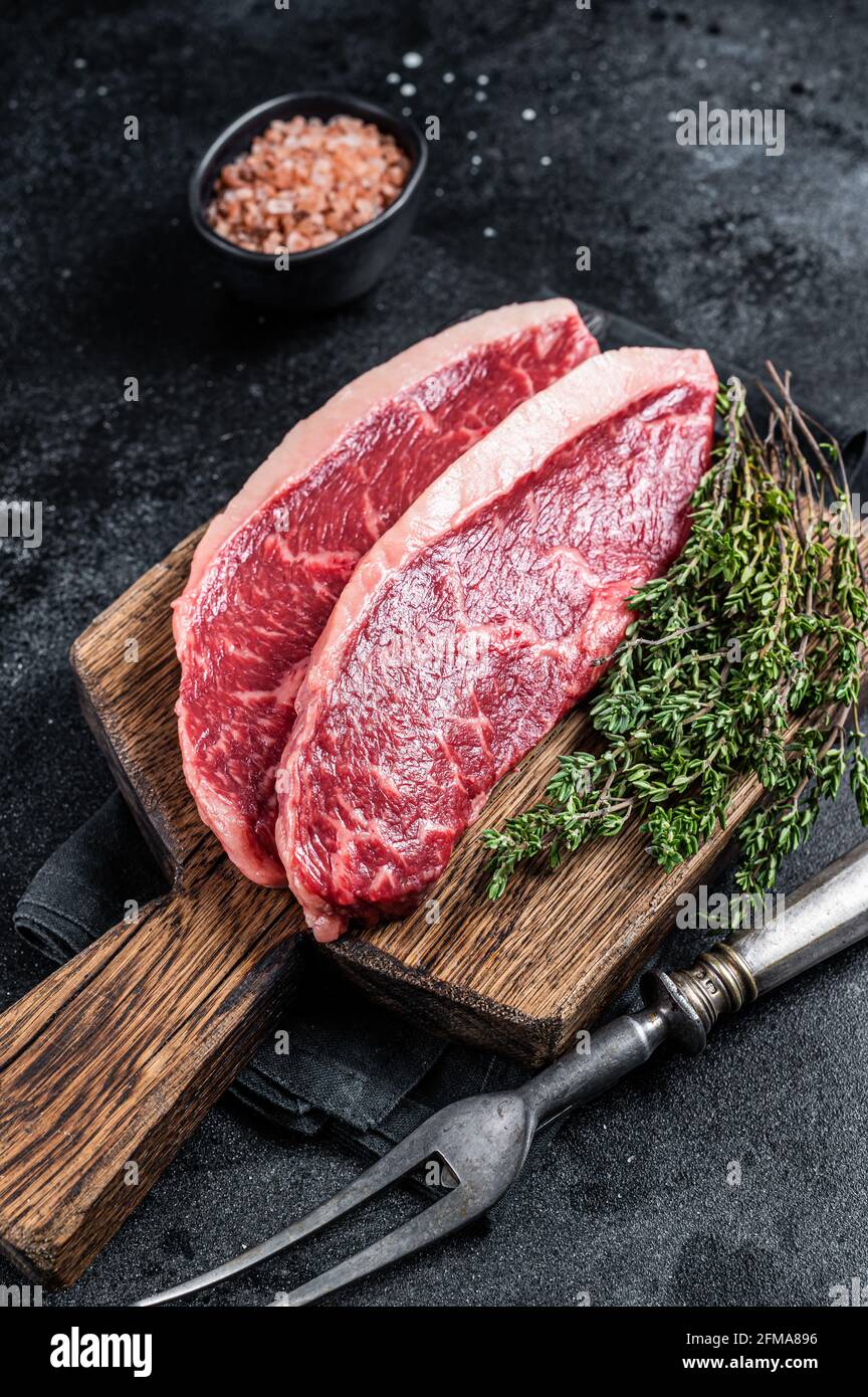 Steak de rumsteck cru non cuit ou biftecks de viande de bœuf au chapeau de sirloin sur une planche de bois. Arrière-plan noir. Vue de dessus Banque D'Images