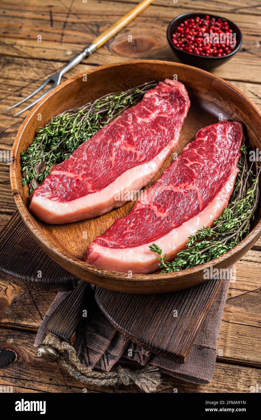 Steaks de viande de boeuf non cuits en haut cru au sommet de sirloin dans une assiette en bois avec des herbes. fond de woden. Vue de dessus Banque D'Images