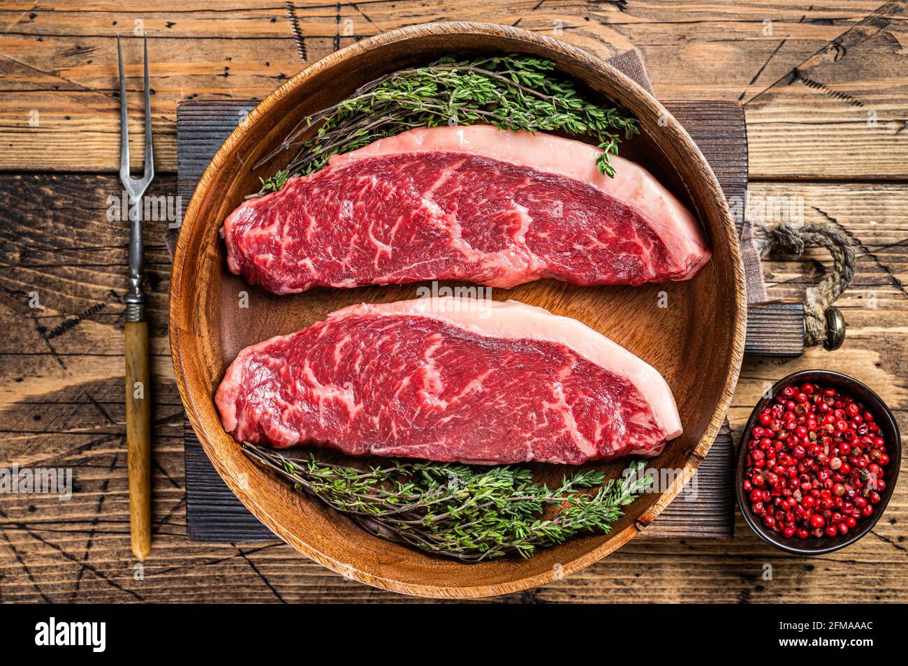 Steaks de viande de boeuf non cuits en haut cru au sommet de sirloin dans une assiette en bois avec des herbes. fond de woden. Vue de dessus Banque D'Images