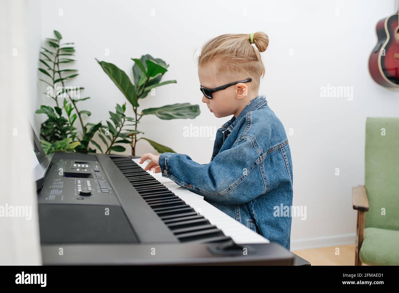 Cool look petit garçon dans des lunettes de soleil jouant du piano  électrique à la maison. Il porte une veste de Jean, ses cheveux blonds dans  un petit pain. Vue latérale Photo