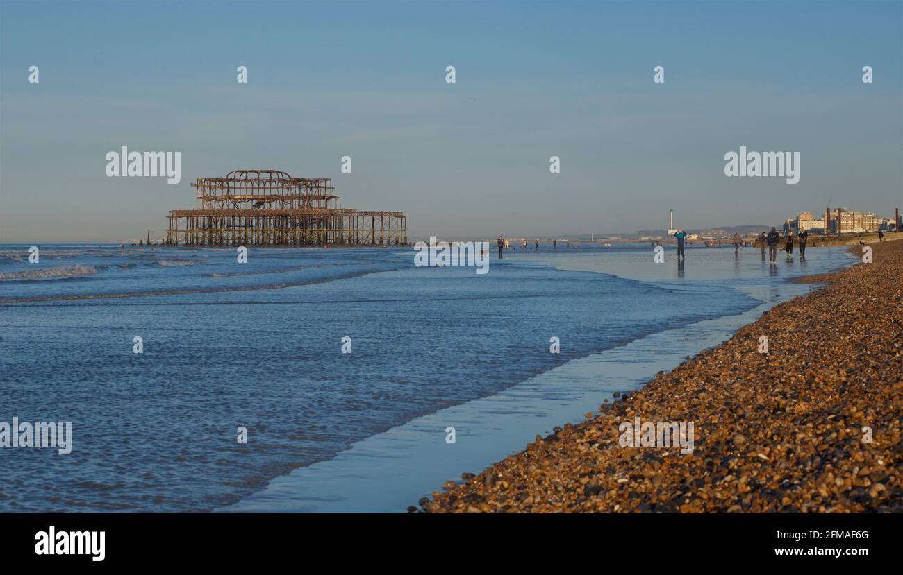 Les gens qui se promènent tôt le matin sur la plage à marée basse, avec les vestiges rouillés de West Pier, un quartier délabré de Brighton. Brighton & Hove, Sussex, Angleterre, Royaume-Uni Banque D'Images