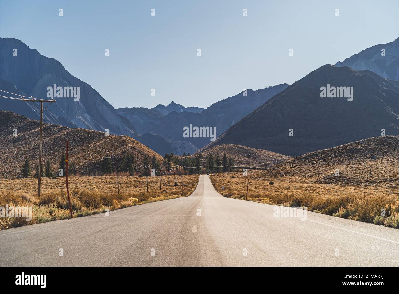 Route à deux voies dans l'aride Sierra Nevada menant à montagnes contre ciel bleu Banque D'Images