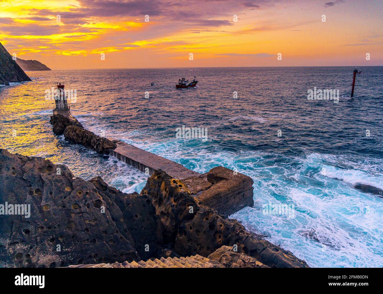 Bateau quittant le phare dans la commune de Pasajes San Juan, Gipuzkoa, Espagne au coucher du soleil Banque D'Images