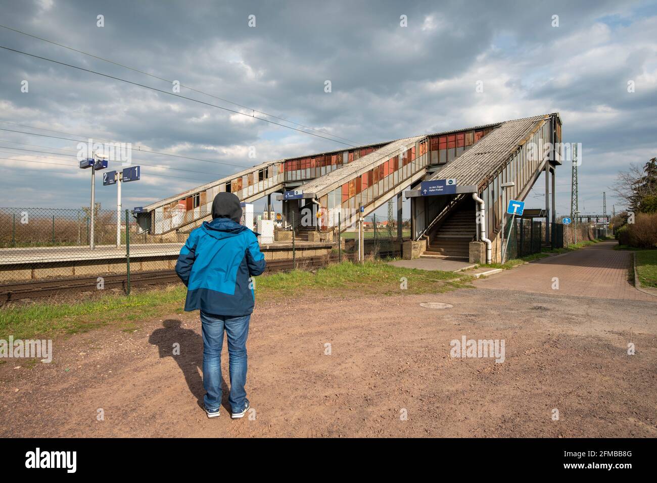 Allemagne, Saxe-Anhalt, Schönebeck, un homme se tient dans une gare abandonnée devant un passage piéton rouillé et couvert. Banque D'Images