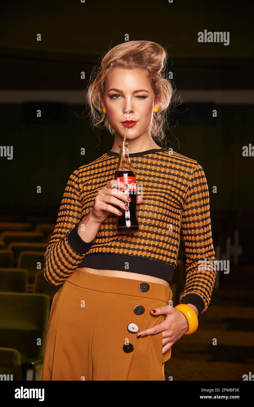 Jeune femme blonde de style rétro avec bouteille de coke au cinéma chambre Banque D'Images