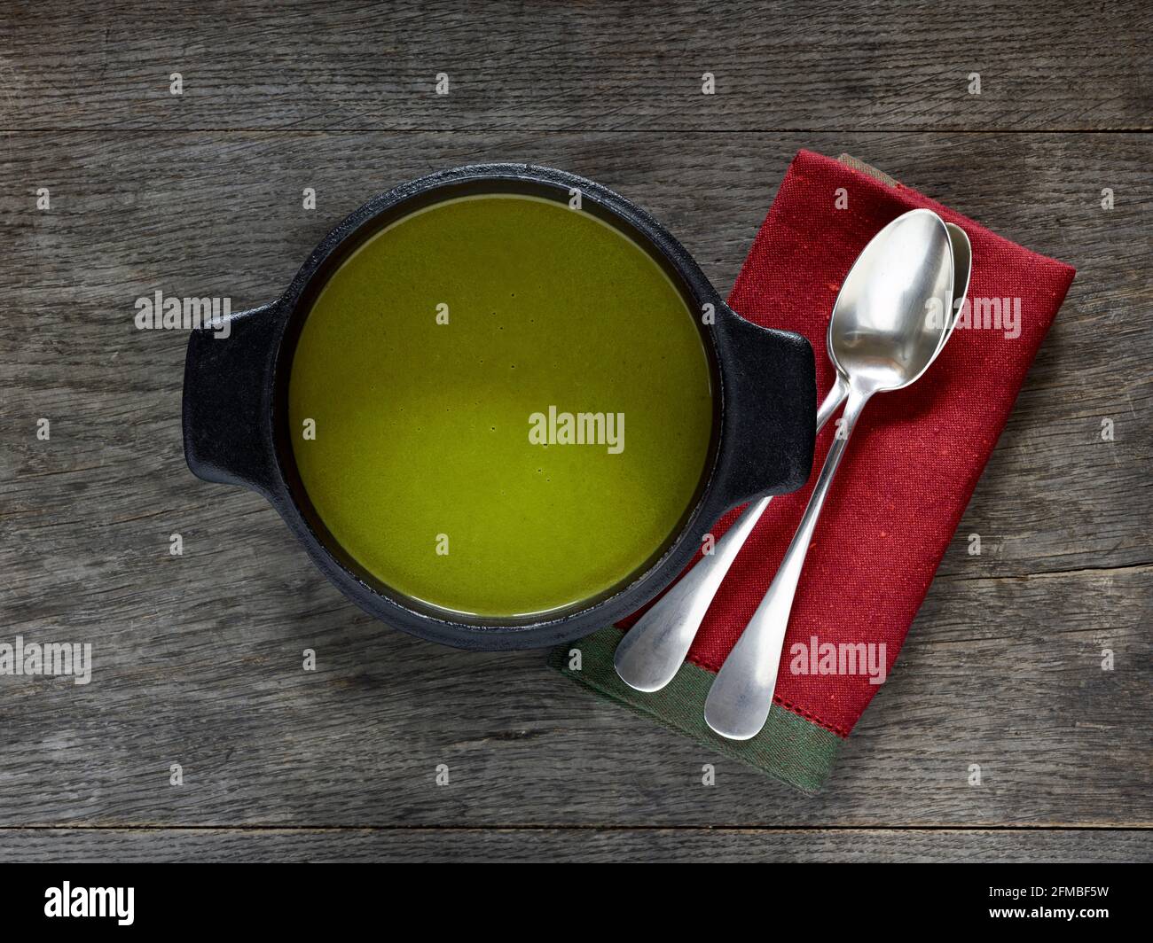 Cuisine ayurvédique - soupe de feuilles de chou-rave dans une casserole noire en fonte sur une table en bois, à côté d'une serviette rouge et de deux cuillères à soupe argentée Banque D'Images