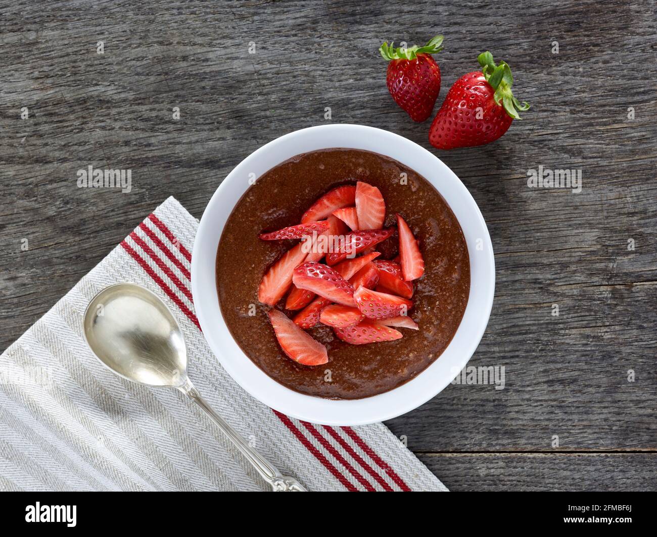 Cuisine ayurvédique - polenta de cacao avec pièces de fraise dans un bol en porcelaine blanche sur une table en bois Banque D'Images