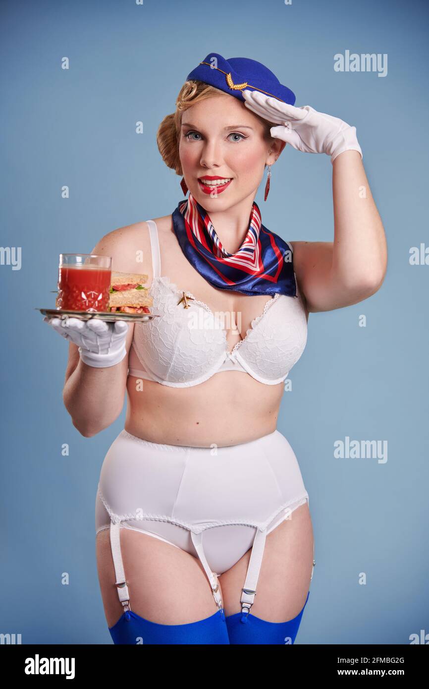 Jeune femme blonde en tant qu'hôtesse dans le regard de pin-up plateau avec jus de tomate et sandwich Banque D'Images