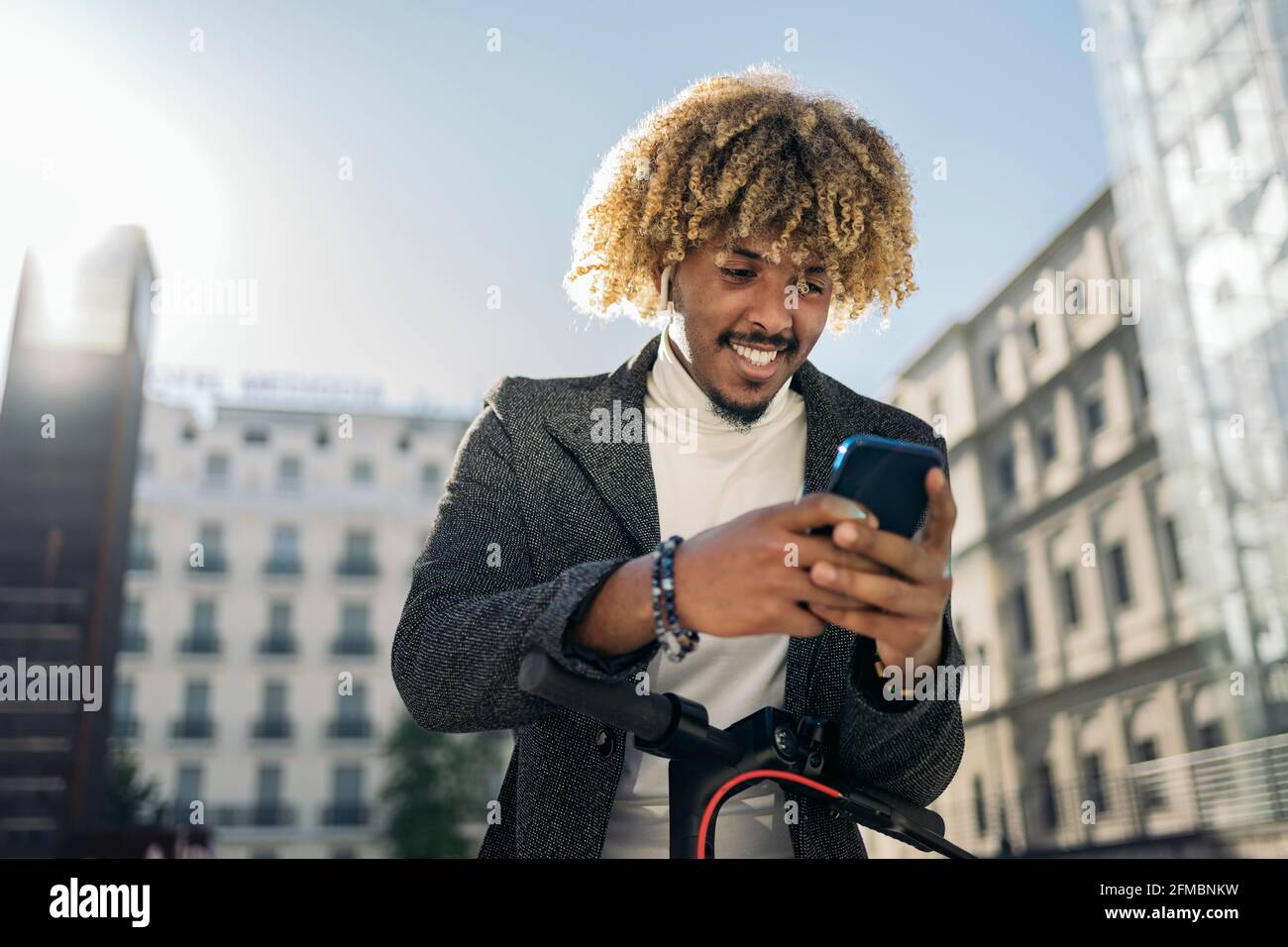 Beau homme africain intelligent dactylographiant téléphone mobile dans la rue dans un scooter électrique. Concept de communication Banque D'Images