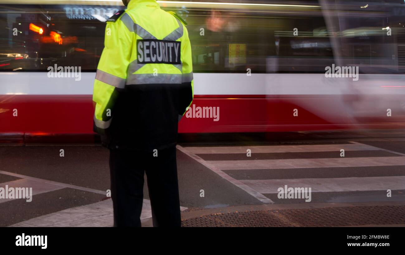 Vue d'un agent de sécurité qui patrouille dans une rue et une ville fréquentées avant le coucher du soleil. Banque D'Images