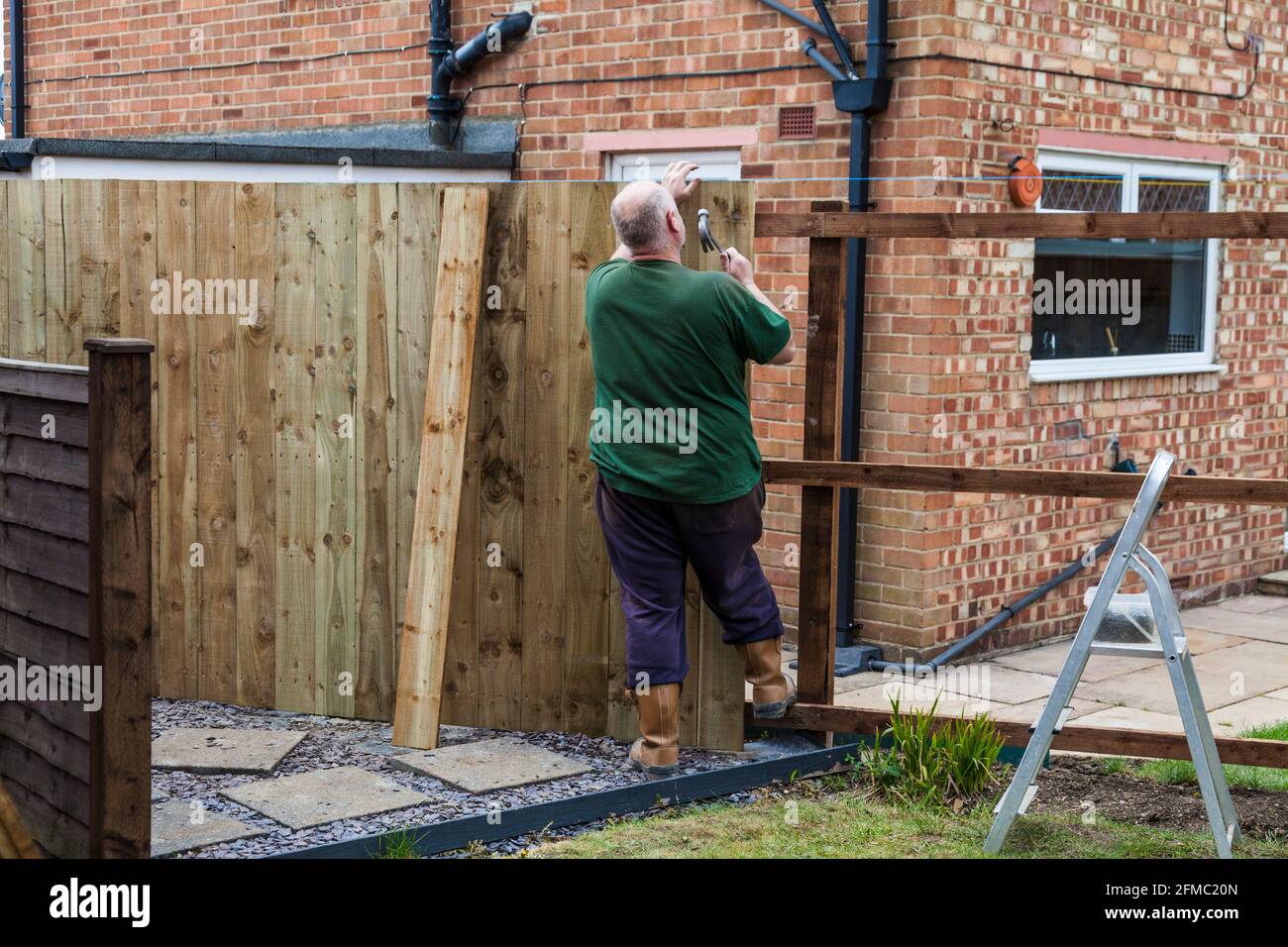 Un homme martelant des clous dans une barrière de panneau et de rail Il vient d'être érigé dans un jardin à Stockton on T-shirts, Angleterre, Royaume-Uni Banque D'Images