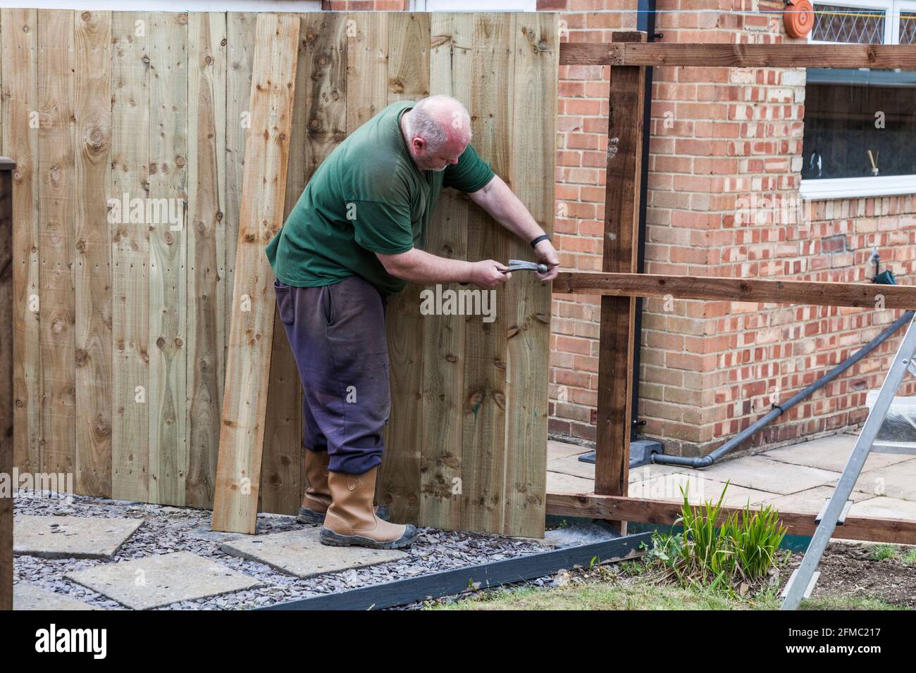 Un homme martelant des clous dans une barrière de panneau et de rail Il vient d'être érigé dans un jardin à Stockton on T-shirts, Angleterre, Royaume-Uni Banque D'Images