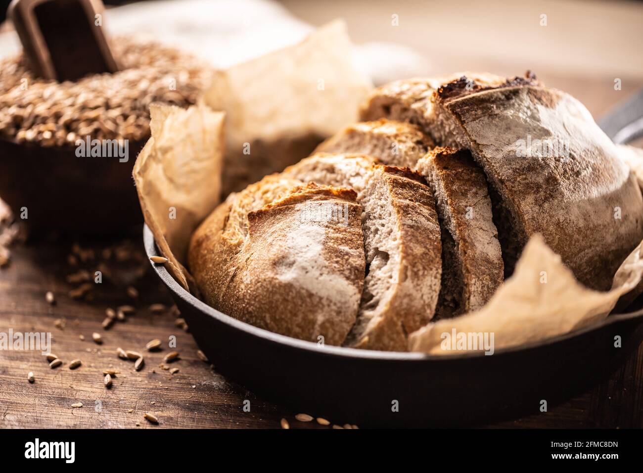 De jolies tranches de pain croquantes servies sur le papier de cuisson dans la poêle rustique en alliage sur la table en bois avec des grains de blé entier en arrière-plan. Banque D'Images