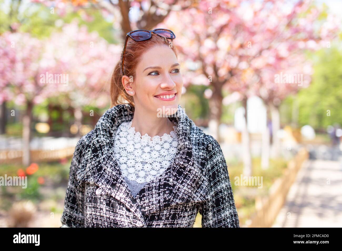 Jeune femme caucasienne positive regardant loin pendant la marche en public parc au printemps Sakura Banque D'Images