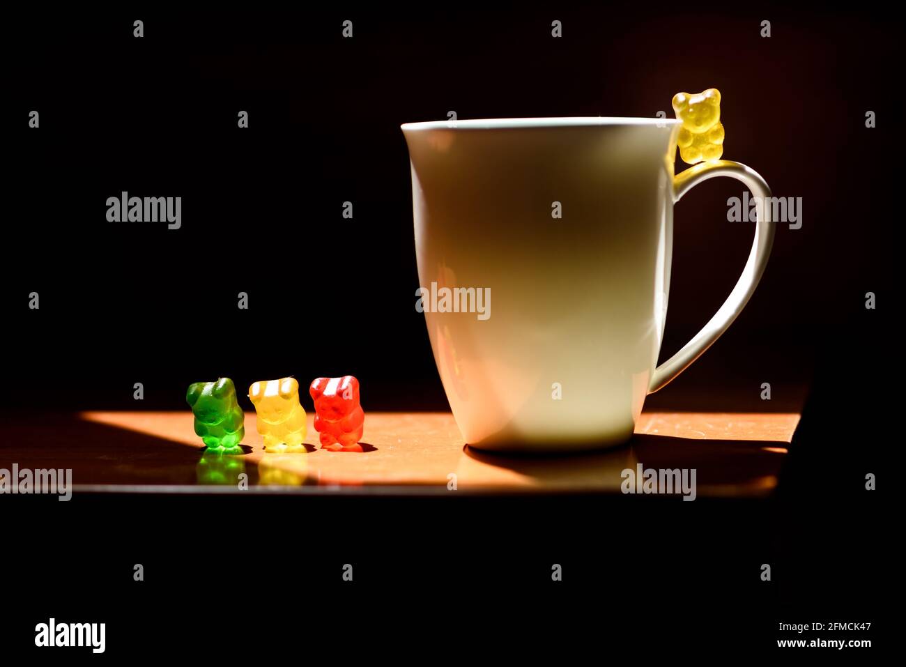 Style Still Life of Gummy Bears sur la table avec lumière directionnelle vive. Image basse avec tasse de lait et friandises colorées. Banque D'Images