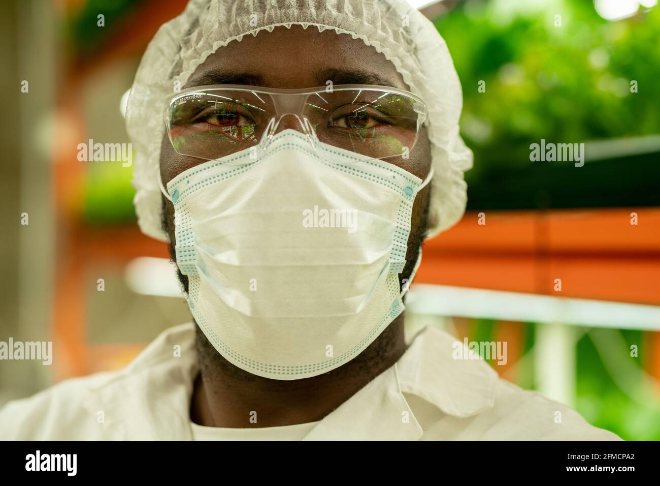 Portrait d'un jeune spécialiste de la culture afro-américaine sérieux en masque, lunettes et casquette debout contre le plateau vertical de la ferme Banque D'Images