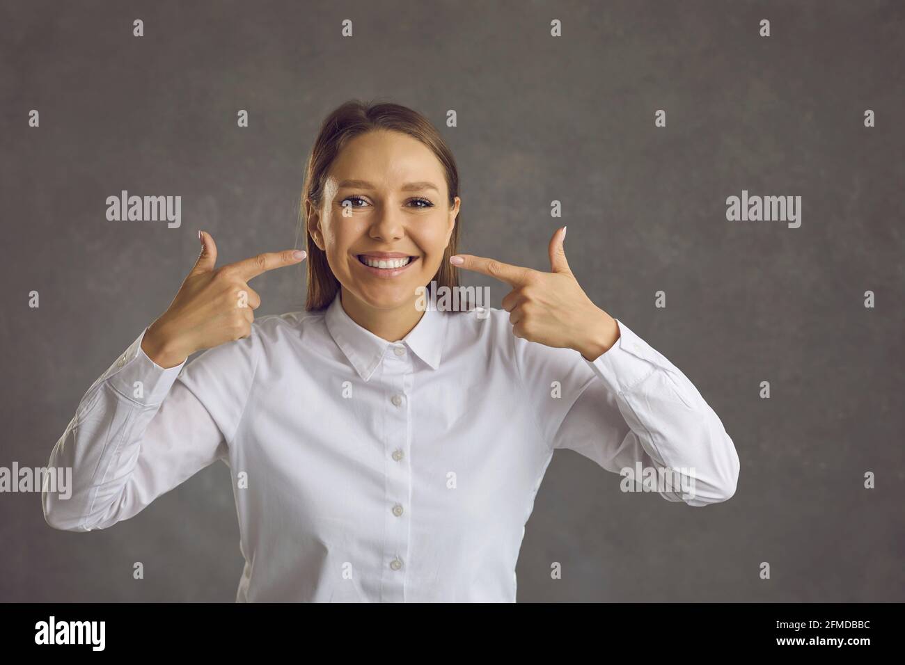Jeune femme pointant avec un double index vers des dents blanches souriez en studio Banque D'Images