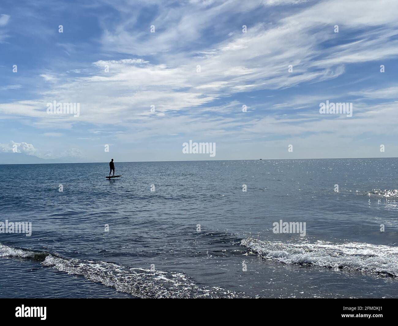 Homme silhoueté à monter sur un panneau électrique de feuille d'aluminium hydrofoil sur un mer sous un ciel nuageux Banque D'Images