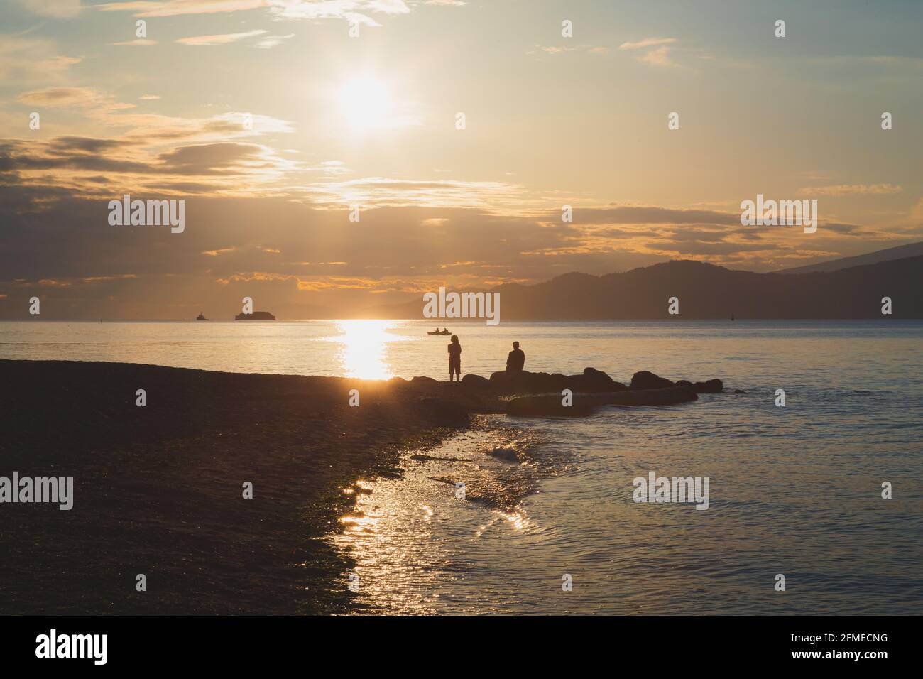 Silhouette de couple pendant l'allumage de la lumière de l'heure d'or au coucher du soleil La côte rocheuse de la plage Spanish Banks Beach à point Gray Une soirée d'été idyllique à Vancouv Banque D'Images