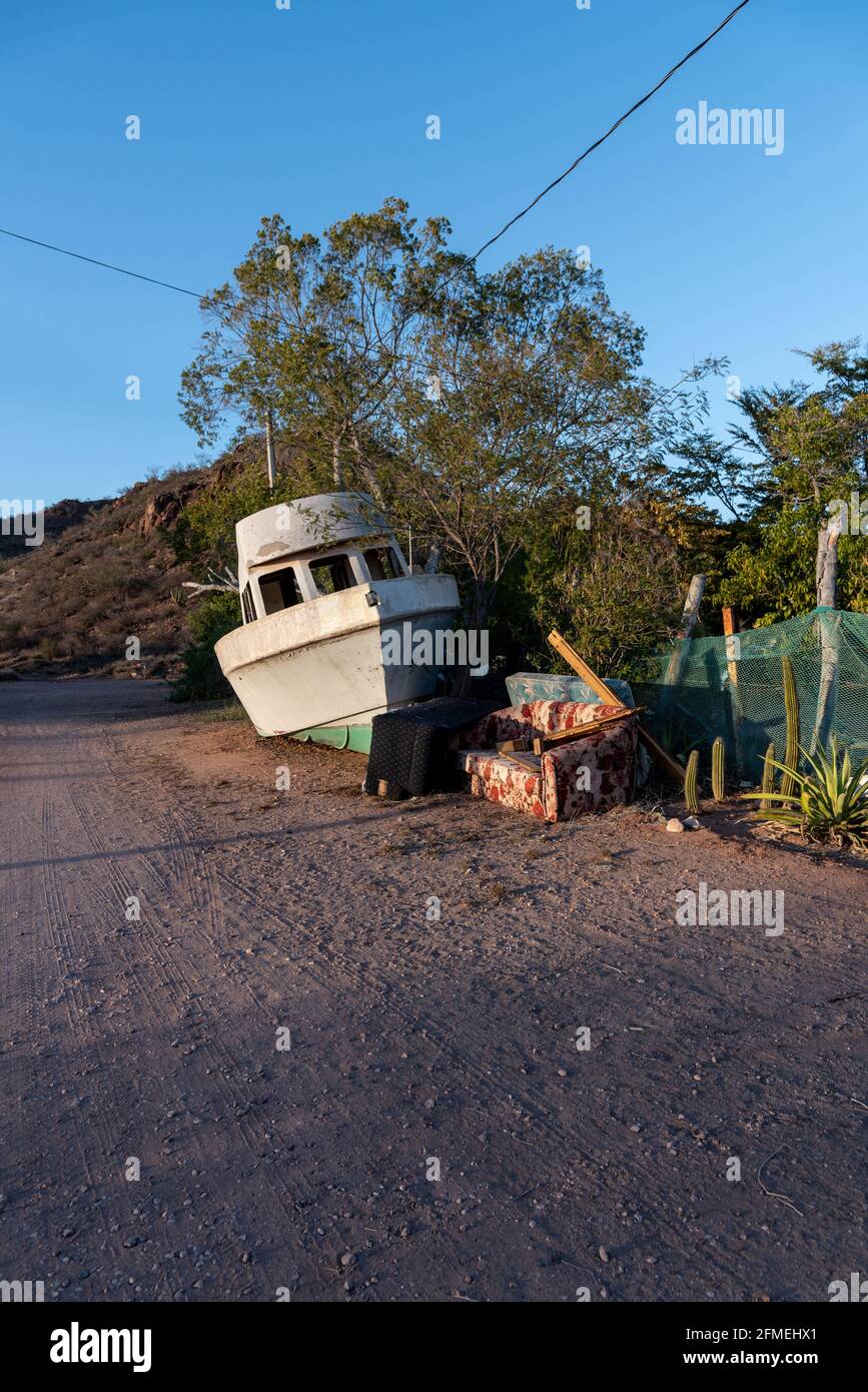 Un bateau de pêche en fibre de verre, un canapé et d'autres articles ménagers soigneusement empilés pour ramasser les déchets sur une route de gravier dans le désert du Mexique. Banque D'Images