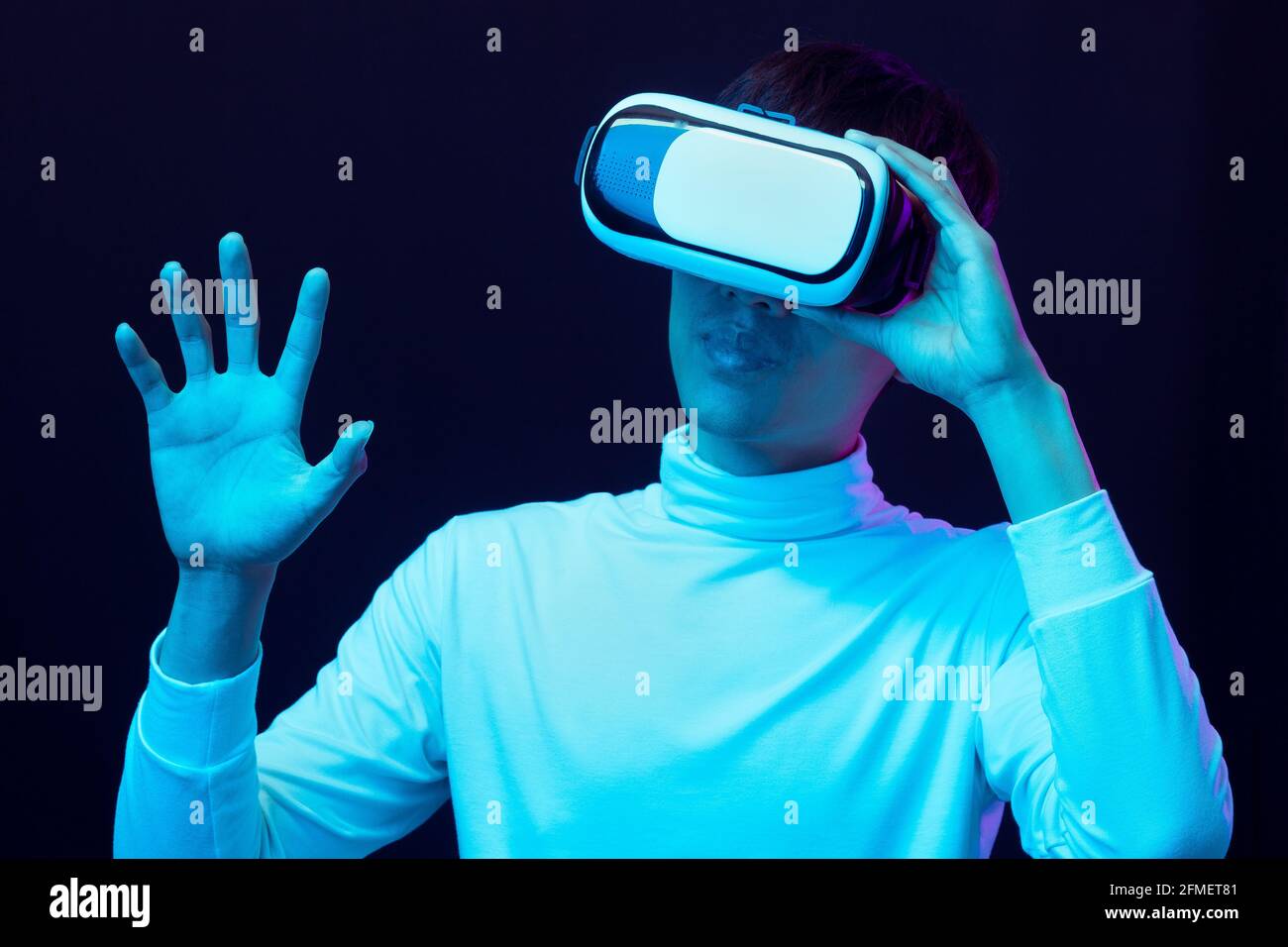 Jeune homme asiatique portant des lunettes de réalité virtuelle regardant une vidéo à 360 degrés dans la lumière de néon, concept de technologie. Banque D'Images Jeune homme asiatique portant des lunettes de réalité virtuelle regardant une vidéo à 360 degrés dans la lumière de néon, concept de technologie. Banque D'Images
