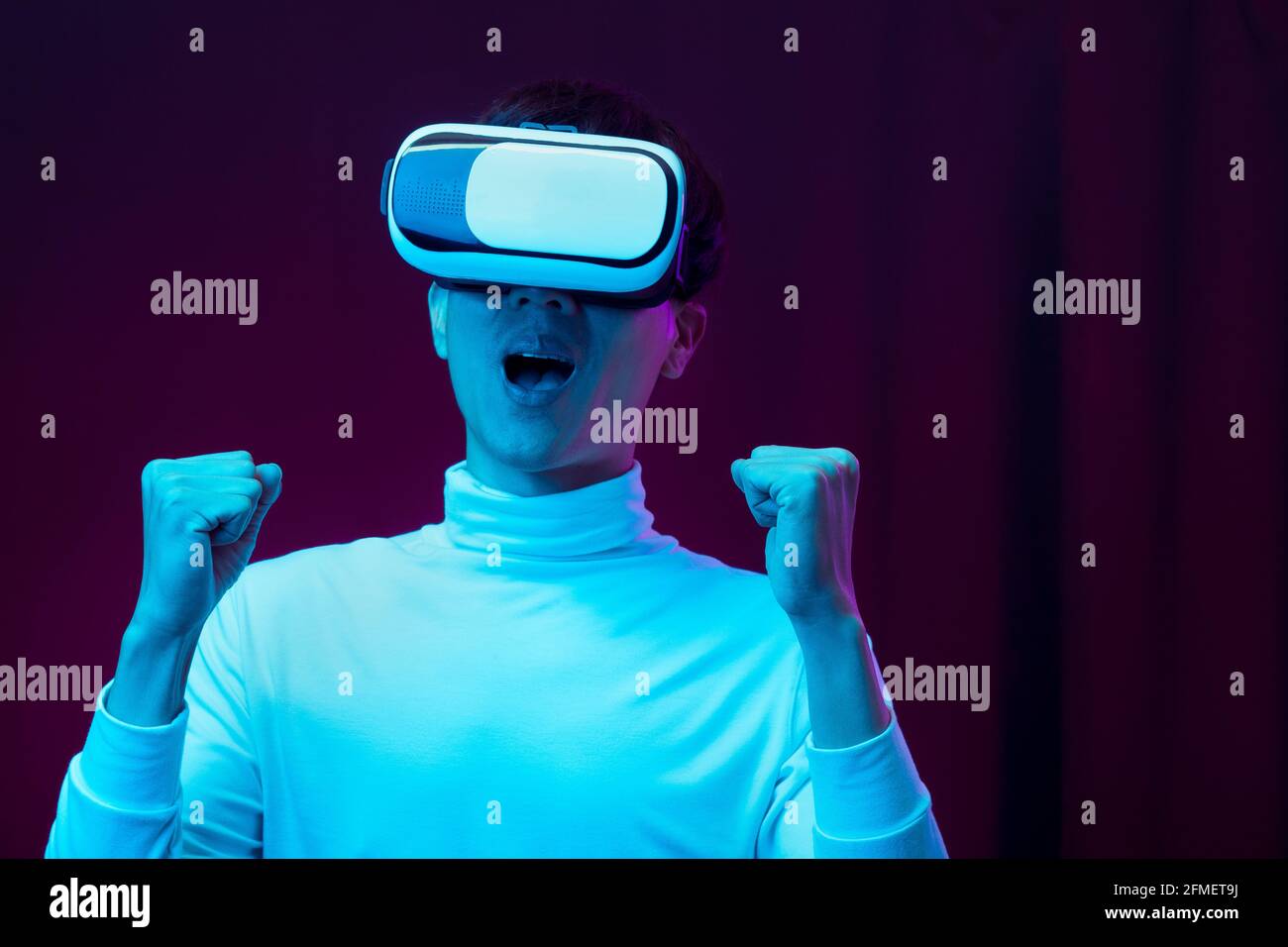 Jeune homme asiatique enthousiaste portant un casque VR à la lumière du néon, concept technologique futur. Banque D'Images Jeune homme asiatique enthousiaste portant un casque VR à la lumière du néon, concept technologique futur. Banque D'Images