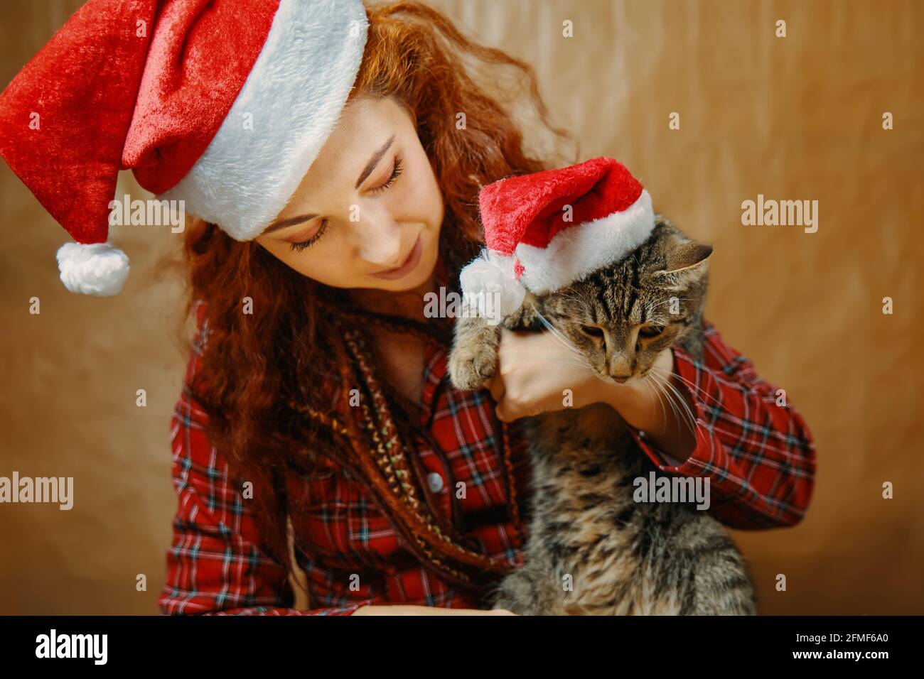 Fille à cheveux rouges en chapeau de Père Noël avec chat en chapeau de Noël.  Femme incroyable avec des dreadlocks en pyjama écossais. L'humeur du nouvel  an. Accessoires de vacances Photo Stock -