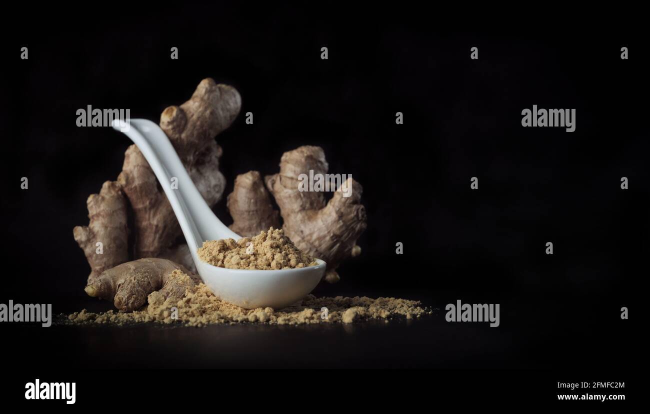 Racine de gingembre et poudre de gingembre dans une cuillère isolée sur fond noir en gros plan sélectif. Banque D'Images