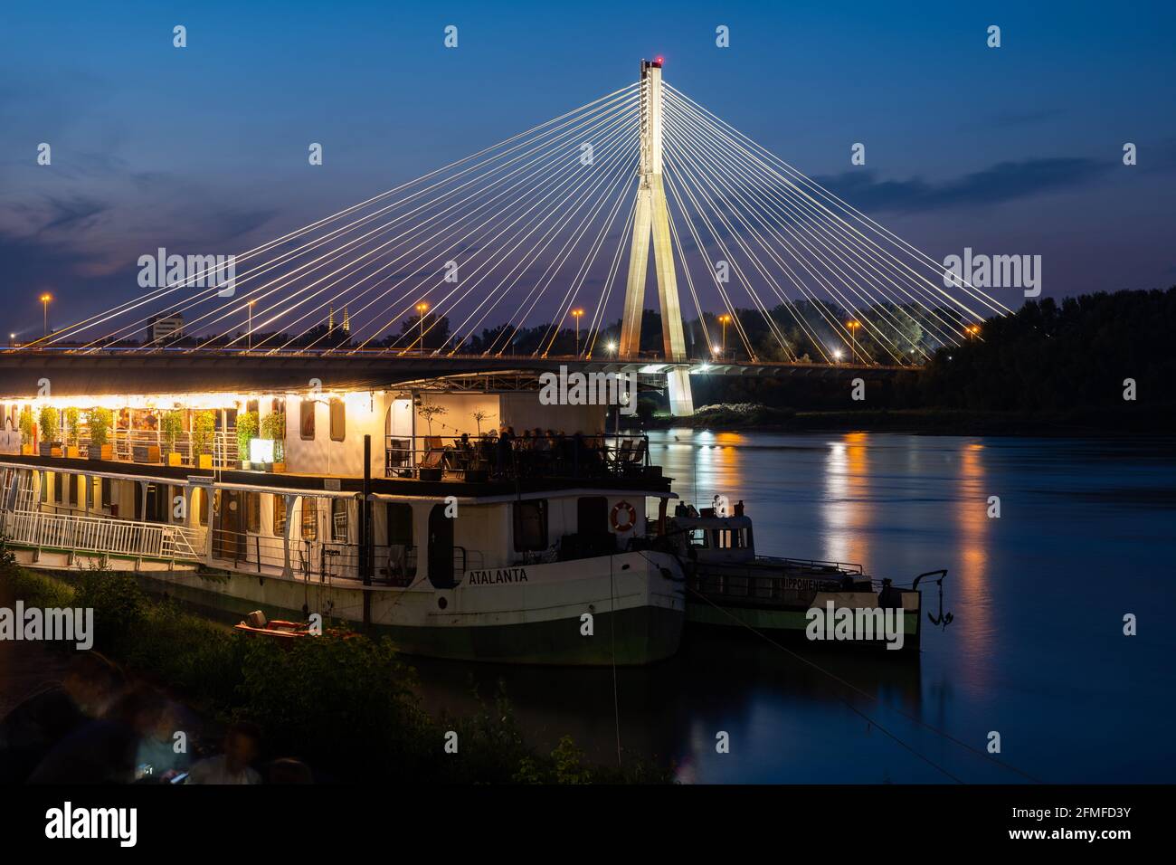 Ville de Varsovie en Pologne la nuit, bateau avec café-restaurant sur la Vistule et pont Swietokrzyski illuminé (pont de la Sainte Croix). Banque D'Images