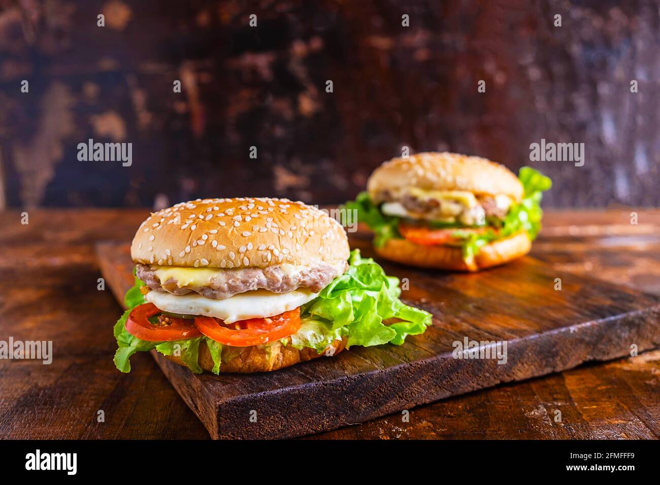 Gros plan de délicieux hamburgers maison frais avec laitue, fromage, oignon et tomate sur une planche de bois rustique sur une table en bois Banque D'Images