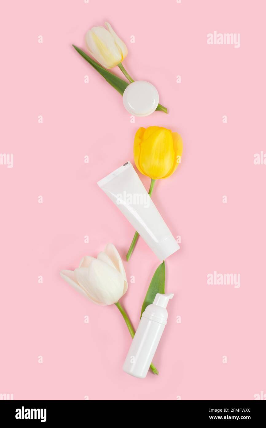 Saint-Valentin et Fête des femmes, concept de fête des mères. Vider les tubes et les bouteilles blancs avec des tulipes blanches sur fond rose. Flat lay, espace de copie. Banque D'Images