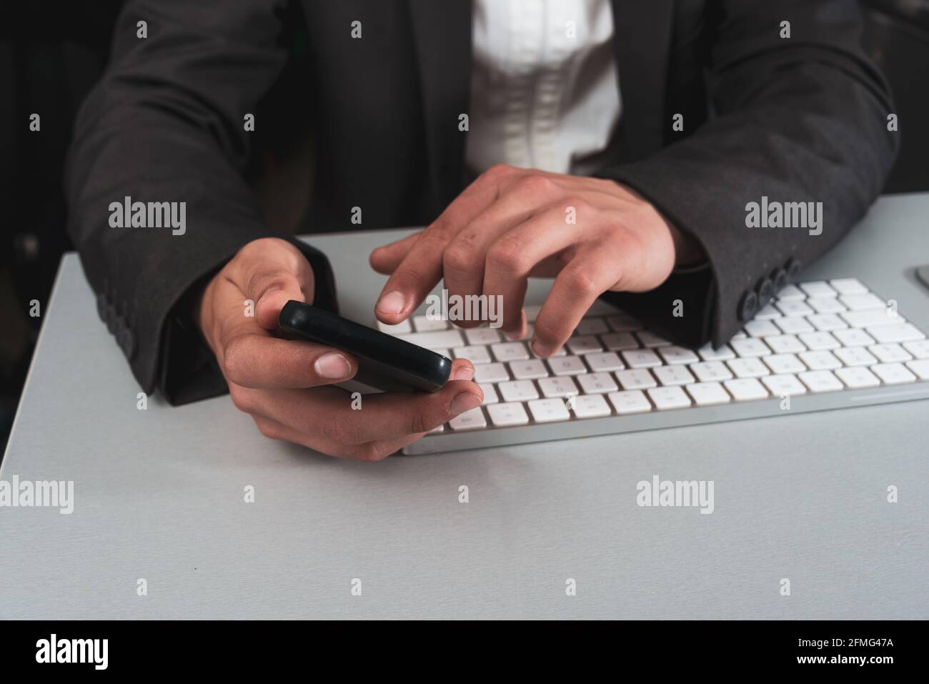 Homme d'affaires mains tenant téléphone mobile avec clavier d'ordinateur, travail à la maison ou surtravaillé concept Banque D'Images