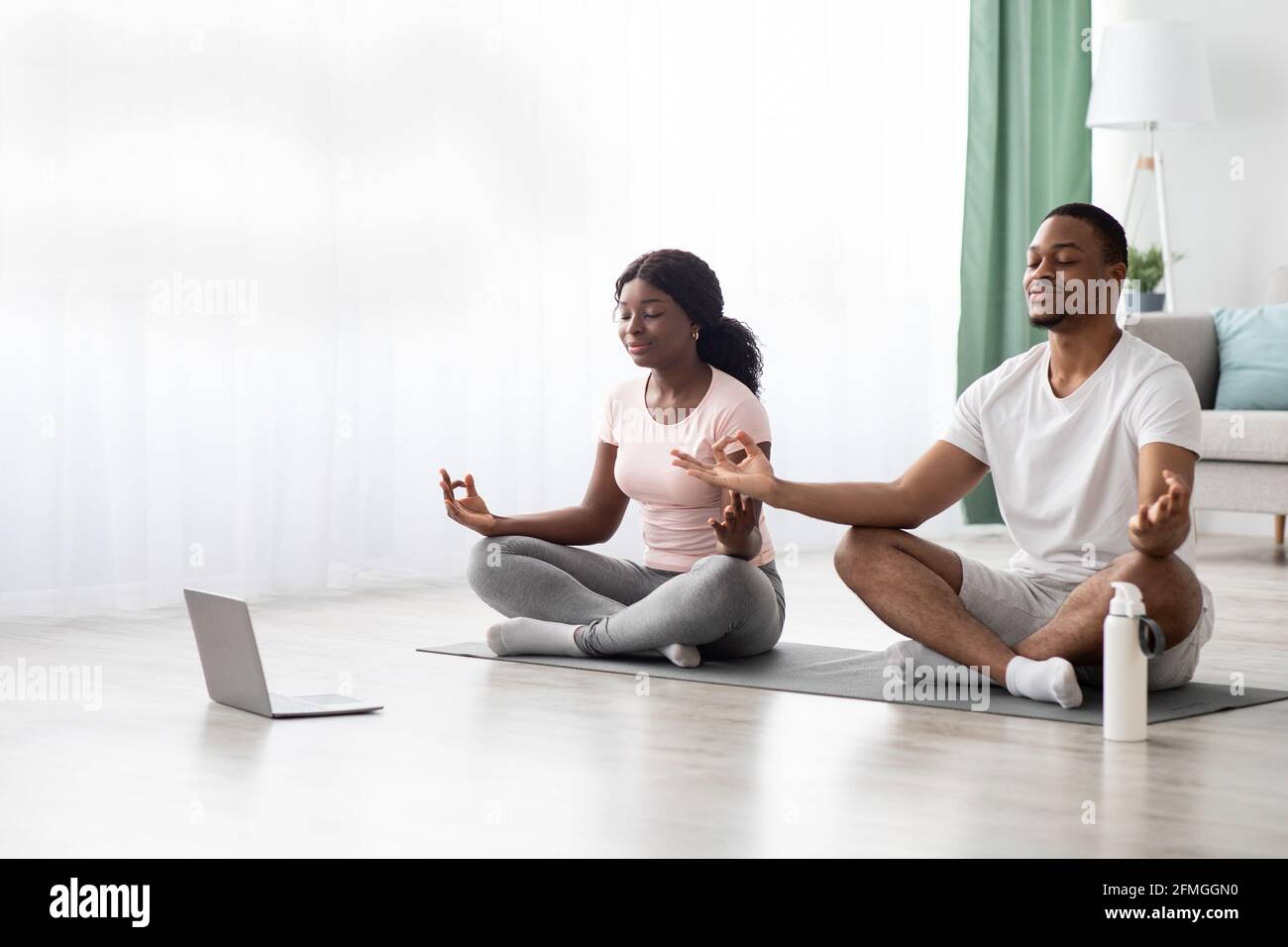 Paisible couple noir méditant à la maison, à l'aide d'un ordinateur portable Banque D'Images