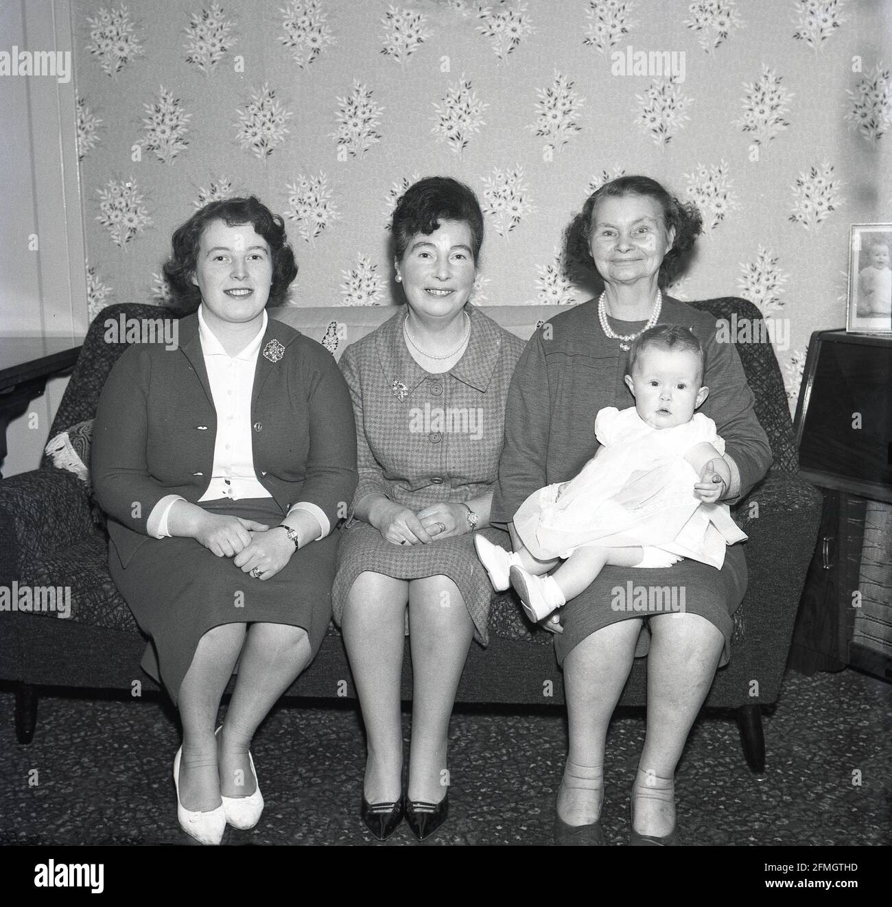 Les années 1960, historique, heureux visages tout autour comme quatre générations d'une famille assis ensemble sur un canapé pour une photo, Kelty, Fife, Ecosse. Nous voyons une arrière-grand-mère sur la droite, sa fille, une grand-mère sur la gauche d'elle, et ensuite sa fille, la mère et le nouveau-né de la mère étant tenu par la grande-grand-mère avec un grand sourire. Banque D'Images