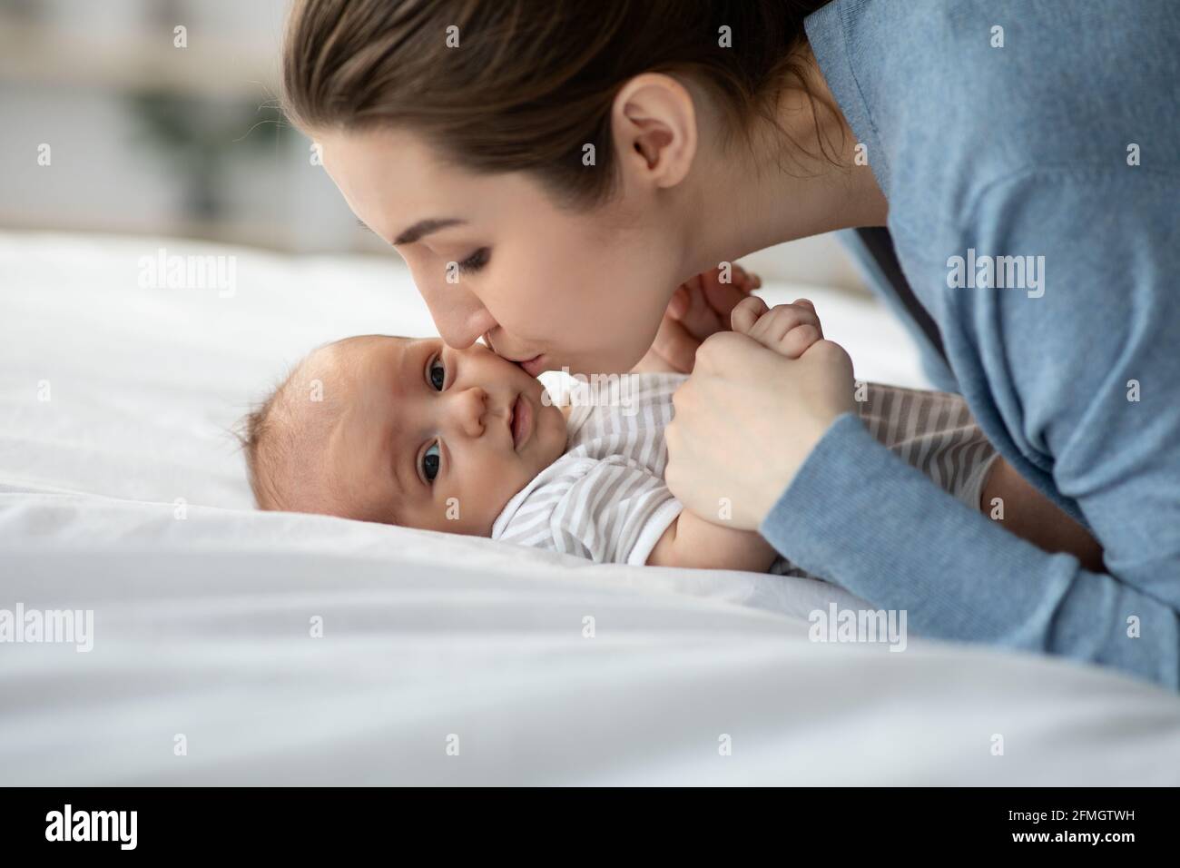 Affectueux jeune maman embrasser son enfant nouveau-né tout en se relaxant Dans le lit Banque D'Images