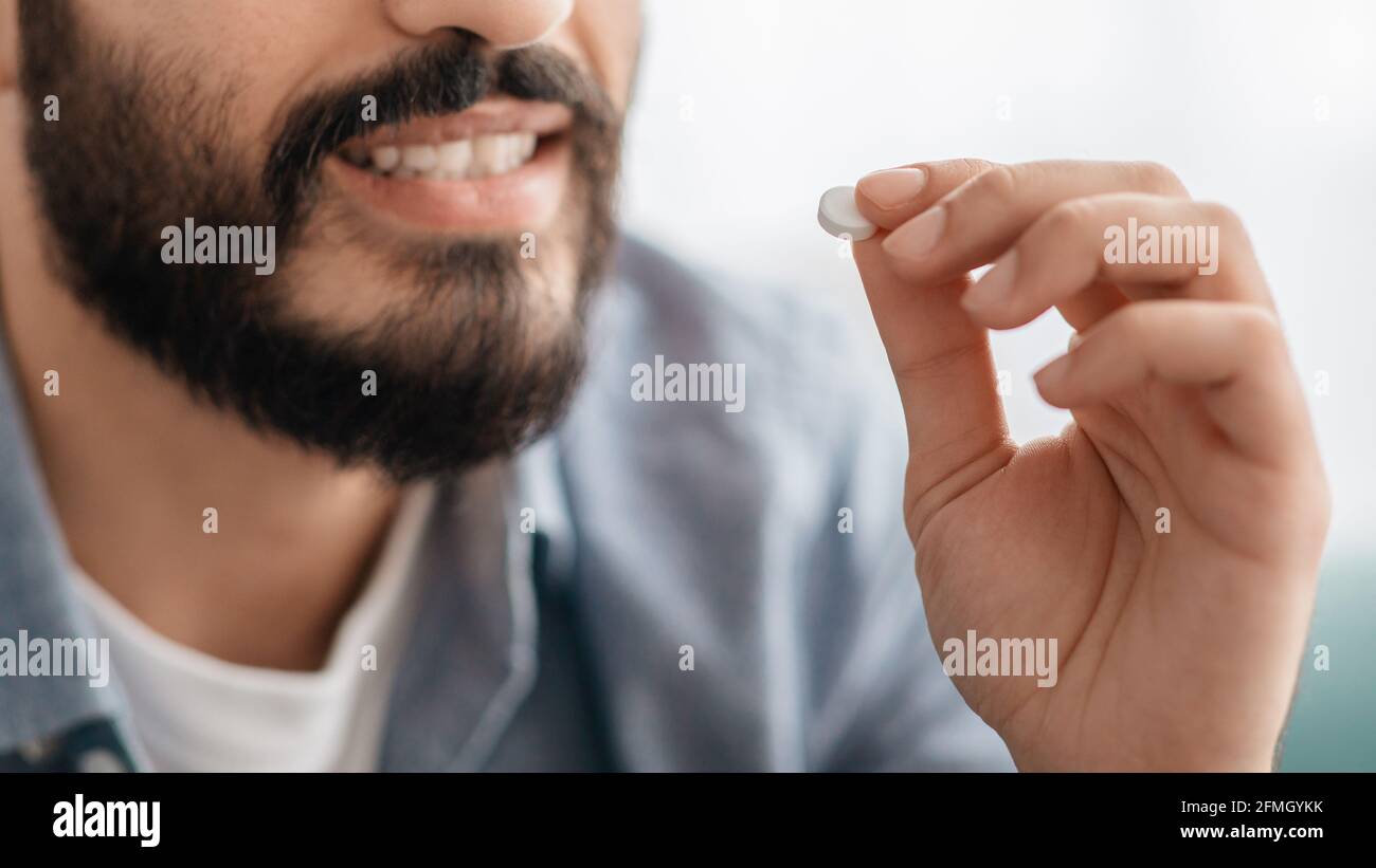 Concept de traitement médicamenteux. Homme barbu souriant non reconnaissable prenant la pilule, court, gros plan Banque D'Images